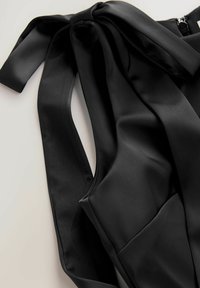 Melns satīna tops ar tauriņa kaklasaites detaļu uz kakla, gludu tekstūru, regulējamiem siksnām un rāvējslēdzēju aizdari aizmugurē.