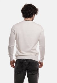 Maglione bianco a maglia con collo rotondo, vestibilità slim e maniche lunghe, abbinato a jeans di denim scuri. Nessun motivo o accento visibile.