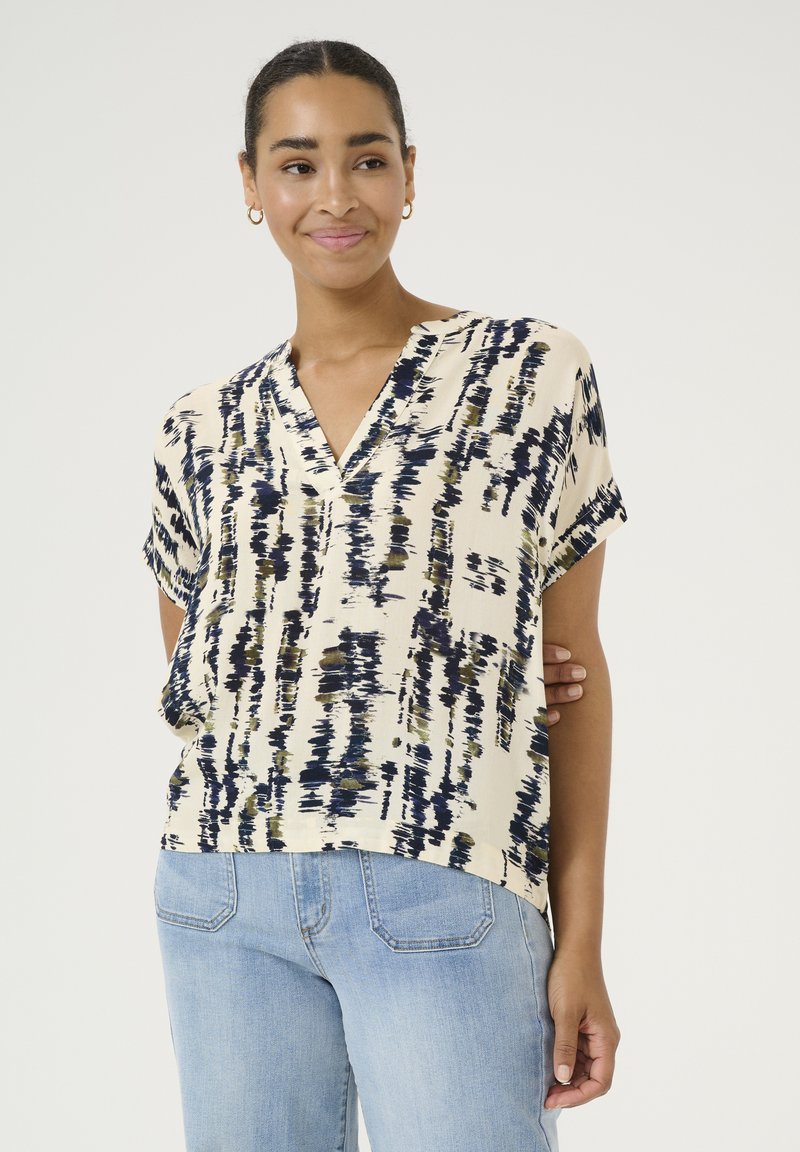 Blouse à manches courtes et col en V avec un imprimé abstrait bleu marine et olive sur fond crème ; texture lisse, coupe décontractée.