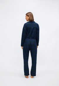 Navy en groene geruite pyjama set met een knoopsluiting aan de bovenkant en elastische tailleband bij de broek. Stof heeft een zachte textuur en een relaxte pasvorm.