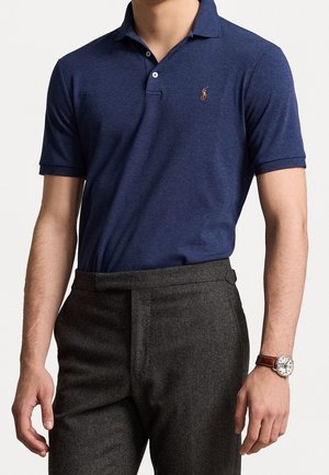Navyblauwe polo met een klassieke kraag, korte mouwen en een klein geborduurd logo op de borst, gecombineerd met grijze op maat gemaakte broeken.