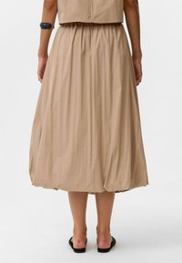 Beige, knielange rok van lichtgewicht, gekreukt stof; heeft een elastische tailleband en plooien aan de zoom, wat een volumineuze vorm creëert.