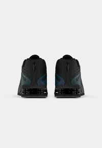 Scarpe da atletica nere con una tomaia textured, supporto per il tallone prominente e una suola lucida multicolore con aperture per la ventilazione.