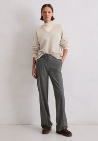 Beżowy sweter z wełny z dekoltem w szpic i podwiniętymi rękawami, połączony z szarymi spodniami w prążki i brązowymi butami. Prosty, ale teksturowany design.