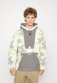 Casaco pullover com capuz em cinza, branco e padrão de camuflagem verde. Apresenta um fecho frontal, um grande bolso e um logotipo na bainha.