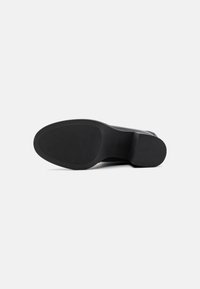 Semelle de chaussure noire avec une surface en caoutchouc texturé, bout arrondi et un faible talon. Le design présente des rainures verticales pour une meilleure adhérence.