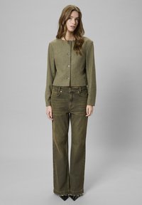 Oliivroheline lühikeste varrukatega kardigan, millel on kolm hõbedast nööpi, koos kulunud, laia jala tumeroheliste teksadega, millel on hõredad servad ja ees olevad taskud.