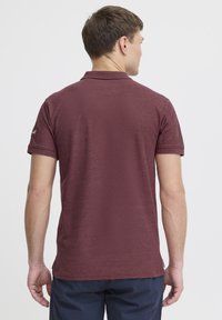 Bordeaux polo t-shirt med korte ærmer, tekstureret stof og et lille logo på ærmet. Klassisk krave og standard pasform.