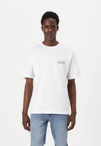 Hvid bomulds t-shirt med korte ærmer, en rund halsudskæring og en lille grøn grafik tekst "Cancun" på venstre side.