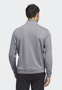 Polo à manches longues, en tissu gris avec une finition texturée, doté d'un col classique et de poignets ajustés. La vue arrière montre une coupe décontractée.