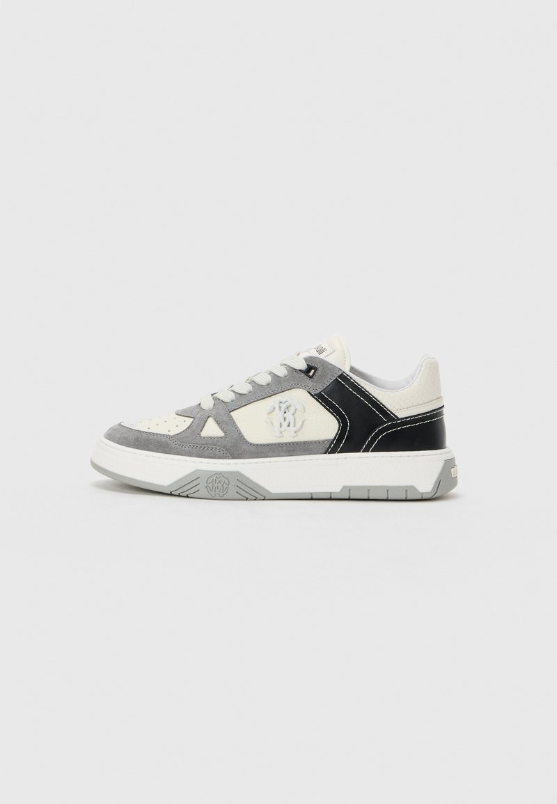 Sneaker low-top in bianco, camoscio grigio e pelle nera con lacci bianchi e ricamo del logo sul lato, esposta su uno sfondo neutro.