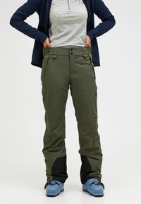 Olijfgroene waterdichte broek met zwarte accenten aan de onderkant, voorzien van een knoopsluiting en zijzakken, gemaakt van duurzame, gladde stof.