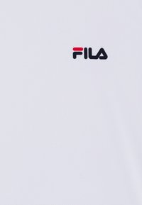 T-shirt blanc à manches courtes en tissu texturé, arborant un logo Fila noir avec une touche de rouge.
