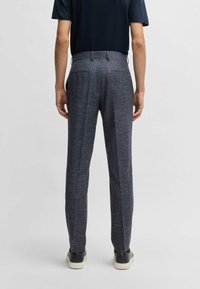 Tailored dark blue trousers with a textured fabric, featuring a fitted waist and two back pockets, paired with black shoes.