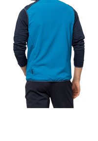 Blå jacka med texturerade marinblå ärmar, med en stilren design och lättviktig tyg. Inkluderar sidofållar för flexibilitet i rörelsen.