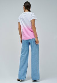 Camiseta de algodón en blanco que se desvanece a rosa, con mangas cortas y un pequeño parche en la parte de atrás. Combinada con jeans de pierna ancha de color azul claro.