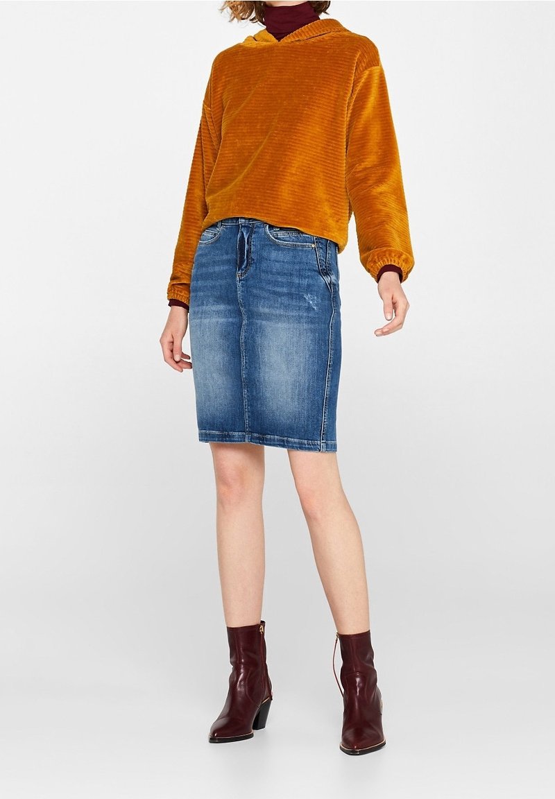 Haut en velours côtelé orange avec capuche, associé à une jupe en denim bleue de longueur genoux et des bottes de cheville rouge foncé. Comprend des poches et un léger effet usé.