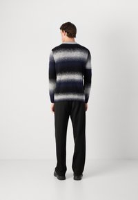 Navy- und grauer gestreifter Strickpullover mit rundem Ausschnitt, ausgestattet mit einer strukturierten Oberfläche und langen Ärmeln, getragen mit schwarzen Hosen.