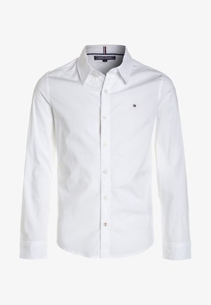 Camisa de manga larga blanca con botones y cuello, que presenta un pequeño logotipo de Tommy Hilfiger en el lado izquierdo del pecho y una etiqueta de marca en el interior del cuello.