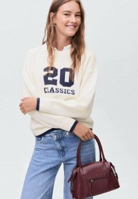 Knit cream sweater with navy accents and "20 CLASSICS" text, paired with light blue denim jeans and a burgundy leather handbag.
