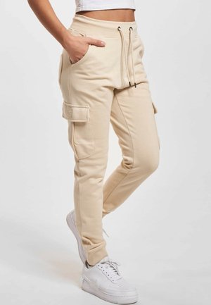 Beige cargo joggerbroek met een aantrekkoort in de taille en klepzakken, gedragen met witte sneakers en een cropped wit topje.