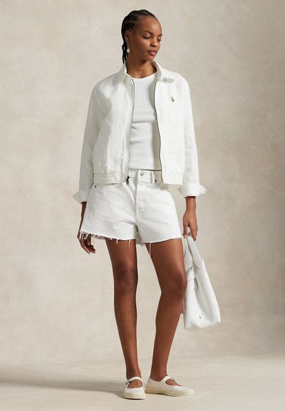 White denim jacket with a zip, white ribbed tank top, frayed white shorts, white flat shoes, and a matching tote bag.