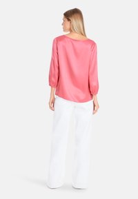 Rosa Satinbluse mit dreiviertellangen Puffärmeln, Rundrücken und lockerer Passform, kombiniert mit weit geschnittenen weißen Hosen. Glatte Textur.