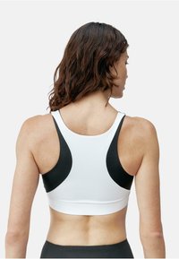 Hvit sports-BH med svarte sidepaneler, med racerback-design og glatt, elastisk stoff. Enkelt tekstur med minimal detaljering.