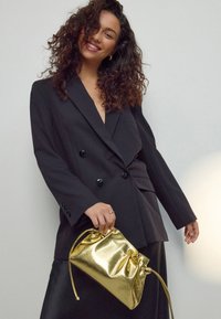 Sacou negru cu design cu două rânduri de nasturi, având nasturi lucioși. Ține un portfard metalic auriu cu o textură încrețită și închidere cu șnur.