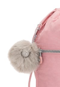 Zaino in tessuto rosa con zip argento e portachiavi a pompon in pelliccia sintetica beige staccabile con un accento a forma di bottone rotondo.