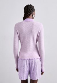 Lilac cardigan with a textured knit design, featuring a collar and ribbed cuffs, paired with matching lilac sequined shorts.