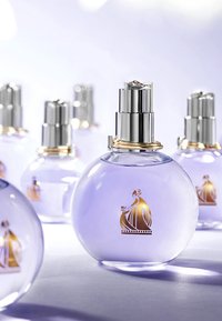 Runda glasparfymflaskor med lavendelfärgad nyans, silverdetaljer, gyllene accenter och en dekorativ illustration av en kvinna i en klänning.