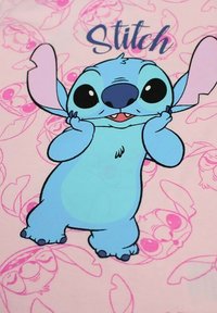 Un fond rose clair met en scène un personnage de dessin animé, Stitch, en bleu avec de grands yeux, souriant, avec des oreilles proéminentes et une pose espiègle.
