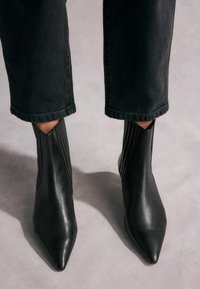 Mustad nahast ankle-boots terava ninaga, ribidega külgpaneelid ja stiilne disain. Kombineeritud lühikeste mustade teksadega.