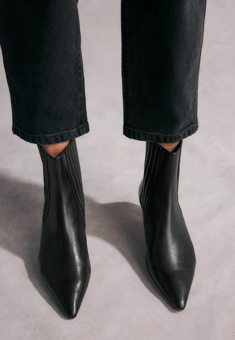 Mustad nahast ankle-boots terava ninaga, ribidega külgpaneelid ja stiilne disain. Kombineeritud lühikeste mustade teksadega.
