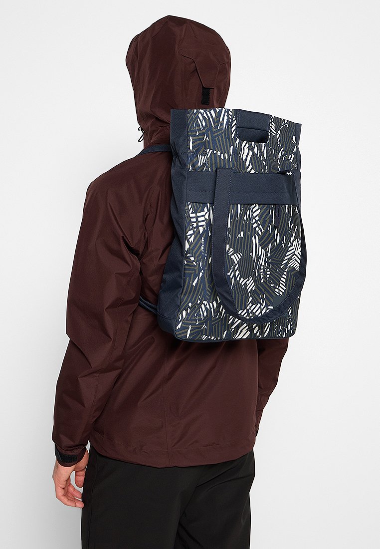 Rucksack mit einem dunkelblauen Grundton und einem weißen und grünen abstrakten Muster, aus strapazierfähigem Material mit verstellbaren Trägern und einem oberen Griff.