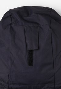 Capuche en tissu foncé avec un rabat rectangulaire et une bande velcro verticale attachée pour le maintien ou l'ajustement.