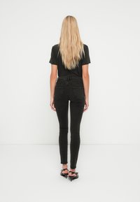 Sorte skinny jeans med høyt liv, jevn denimmateriale og sydd baklommer, kombinert med en ensfarget svart t-skjorte og høye hæler.