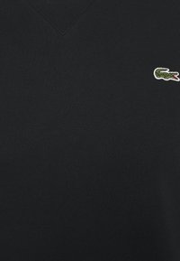 Tissu noir avec un petit logo crocodile vert brodé présentant une bouche rouge ouverte dans le coin supérieur droit.
