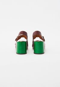 Sandalias de tacón de cuero marrón con cierre de hebilla, que cuentan con tacones en bloque de un verde brillante. Diseño de espalda abierta, textura suave y forma redondeada.