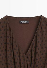 Braunes V-Ausschnitt-Oberteil mit dunklen Polka-Dots, gerafften Stoffdetails und Massimo Dutti Etikett mit der Aufschrift "Made in Morocco".