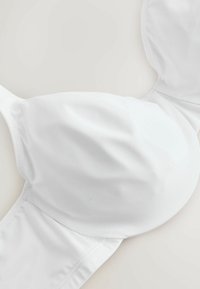 Biały wyściełany biustonosz z fiszbinami i regulowanymi ramiączkami, ułożony na płasko na jasnej powierzchni.