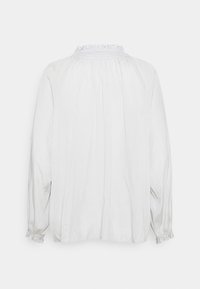Blouse blanche à manches longues avec tissu froncé, col et poignets à volants, vue de dos sur un fond uni.