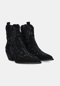 Botines de ante negros con tacones bajos, cremallera lateral y tachuelas decorativas oscuras en patrones en espiral.