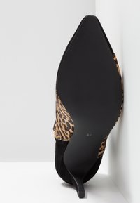 Zapato de tacón de punta negra con estampado de leopardo visto desde la suela, tamaño 37, posicionado contra una pared blanca en la esquina.