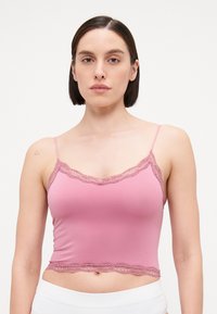 Camisole rose en tissu doux, avec des bretelles ajustables et une finition en dentelle le long de l'encolure et de l'ourlet inférieur. Texture lisse.