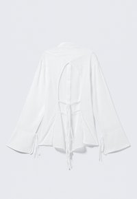 Hvid rygløs skjorte med lange klokkeærmer, der har snorelukning og et åbent, udskåret rygdesign. Glat, let stof.