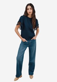 Marineblaues Oberteil mit kurzen Ärmeln aus Spitze, kombiniert mit hellblauen gerade geschnittenen Jeans und beigen Schuhen. Einfaches Design mit lässiger Passform.