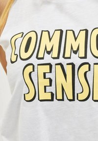 Hvitt bomulls tanktop med tydelig svart og gul tekst som sier "COMMON SENSE." Lett materiale med en avslappet design.