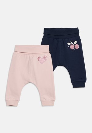 Deux pantalons pour bébé, un rose clair avec un cœur scintillant sur la jambe, et un bleu marine avec un motif cerise scintillant près de la taille.